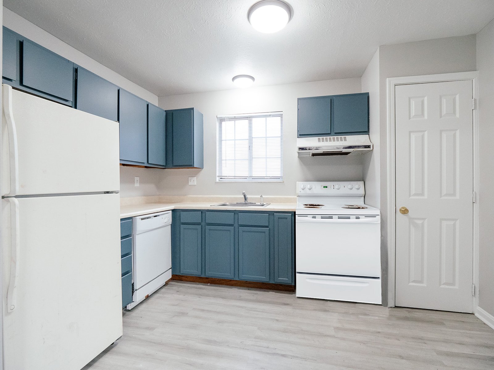 Kitchen with blue cabinets, white appliances, and pale wood-look flooring