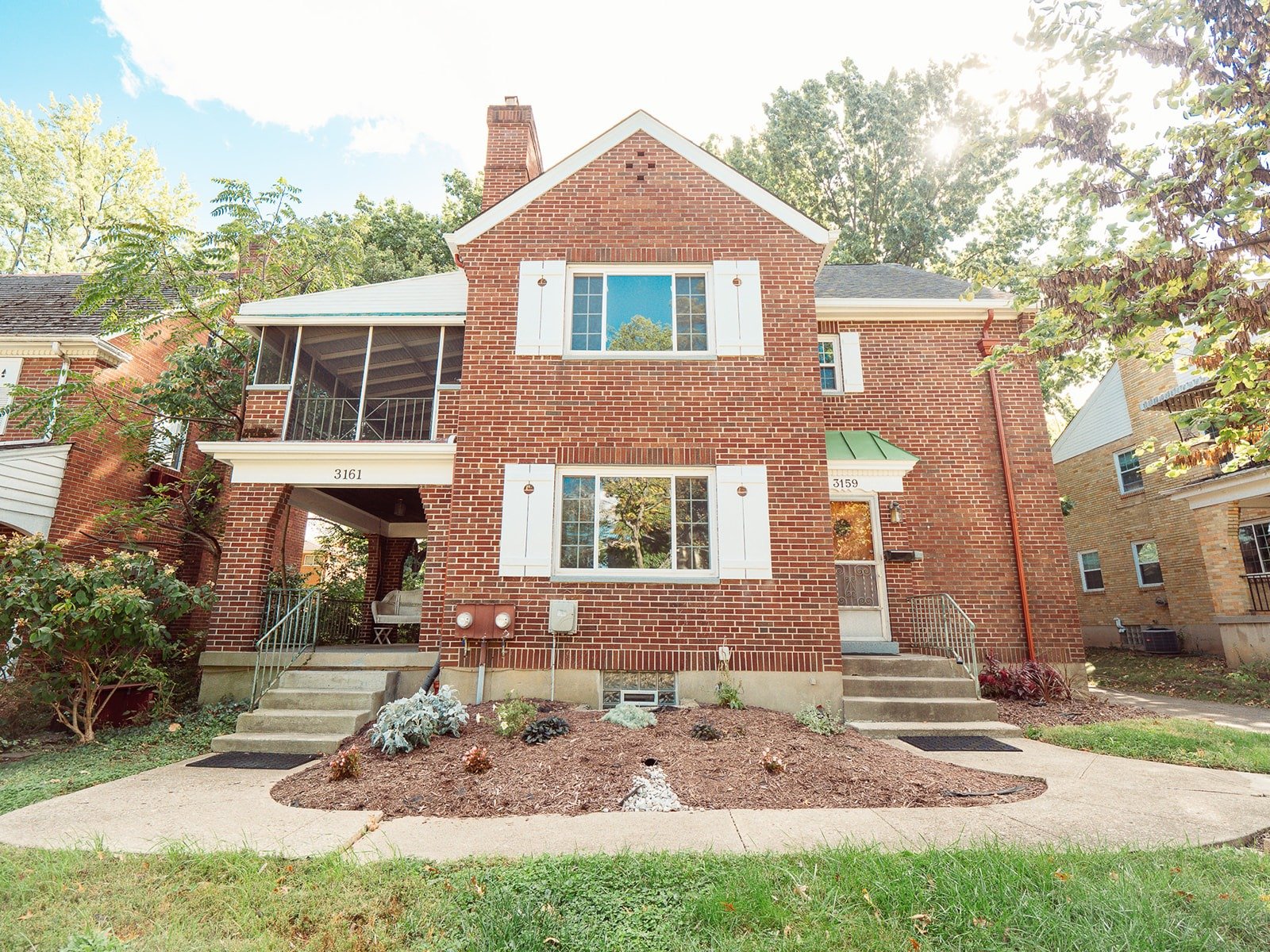 Red brick residential building with white shutters and landscaped front yard