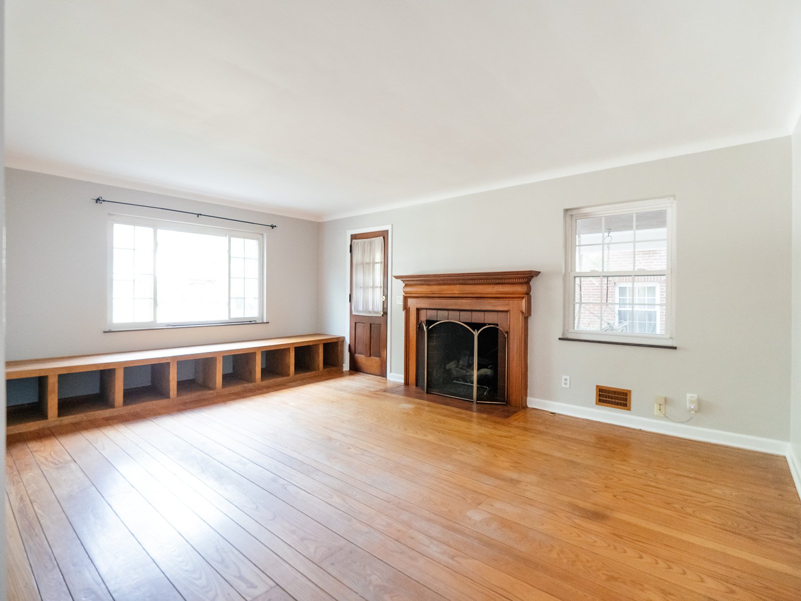 Sunlit living room with a wood mantel fireplace and built-in shelves