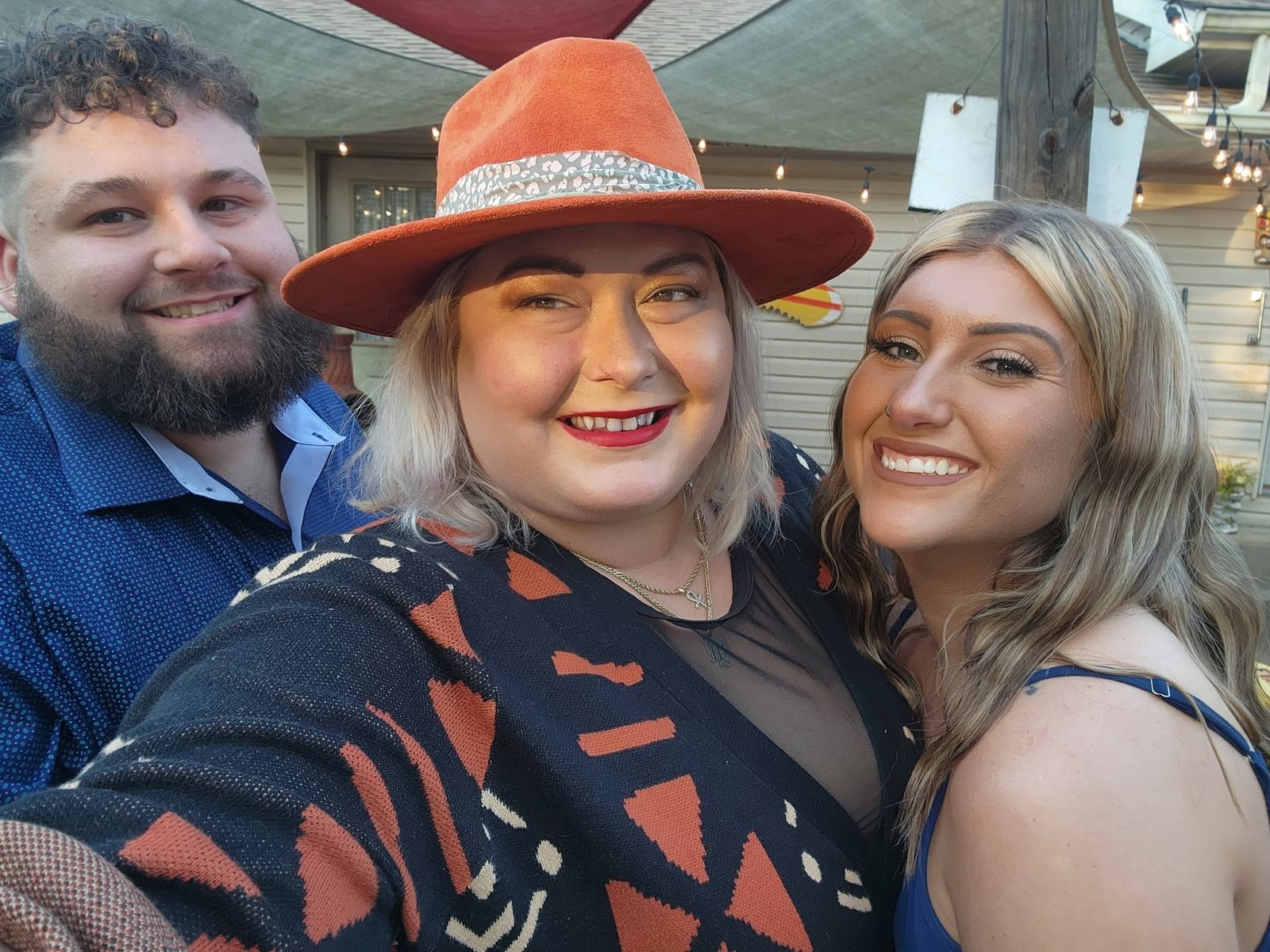 Three friends smiling together, one wearing an orange hat